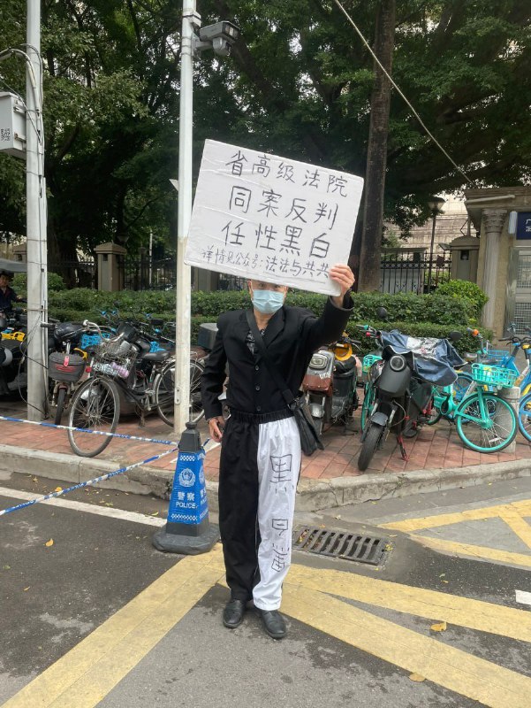12月25日，广东省广州市天河区广东省高级人民法院门前，一名男子身穿讽刺法院“半黑半白、黑白颠倒”的裤子，手举标语牌控诉省高级法院，称其“同案反判，任性黑白”