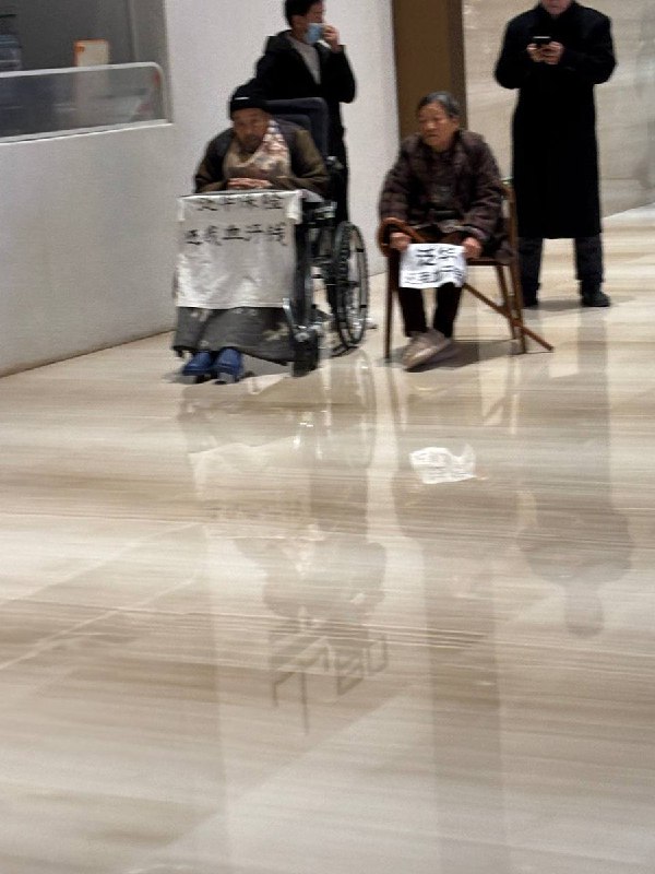 网友投稿：近日，西安市雁塔区禾盛京广中心A座大厅内，一名老人推着另一名坐轮椅的老人举标语维权，标语内容为“泛华保险还我血汗钱”