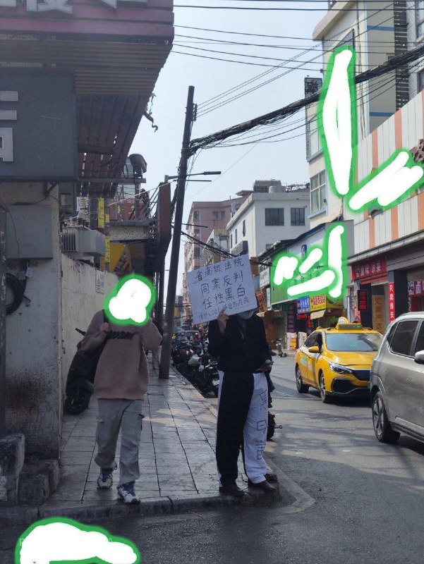 网友投稿：1月28日中午，广州天河，该名男子再次穿着“黑白颠倒，半黑半白”的裤子，举着“省高级法院，同案异判”的牌子在维权