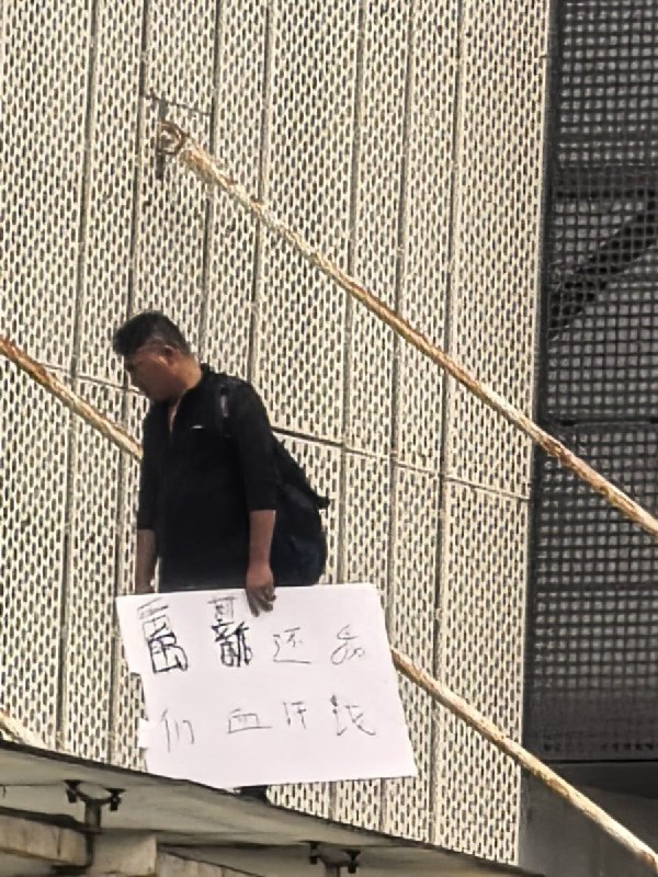 3月23日，广东省深圳市笋岗玩具文具批发市场附近，一名男子站在楼上举着“禹新还我们血汗钱”的牌子跳楼维权