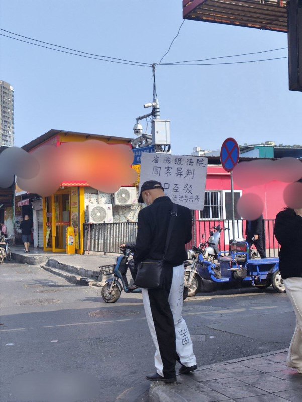 网友投稿：1月28日中午，广州天河，该名男子再次穿着“黑白颠倒，半黑半白”的裤子，举着“省高级法院，同案异判”的牌子在维权