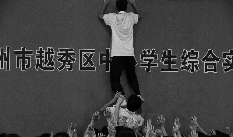 3月20日，深圳光明区实验学校“中考百日誓师大会”现场，学校让女学生们踩着男生的肩膀爬上两米多高的围墙