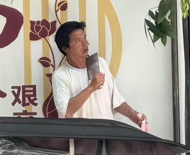 近日，河南太康一超市门口，一名中年男子手持一把菜刀架在自己的脖子上，而在他背后的墙上恰有二字“艰辛”
